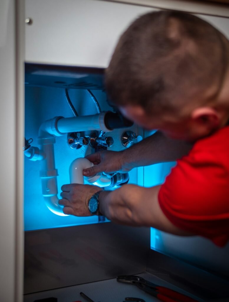 A technician fitting new supply lines under a sink