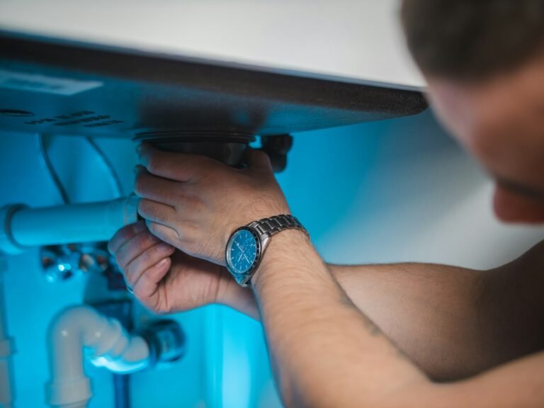 A plumber tightening a fitting under a sink