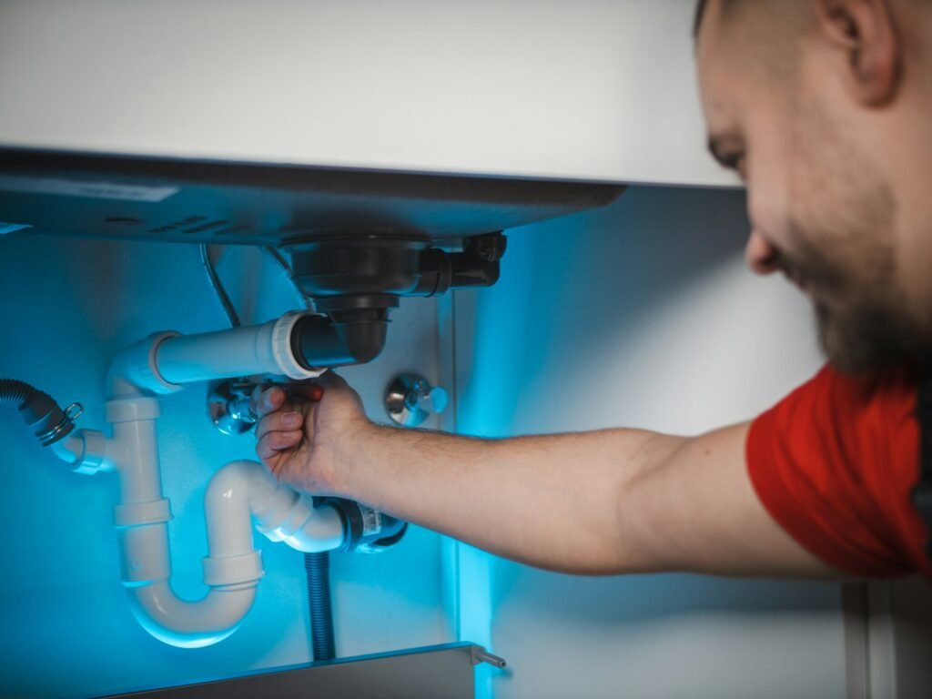 A plumber repairing pipes inside a wall cabinet