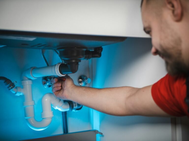 A plumber repairing pipes inside a wall cabinet
