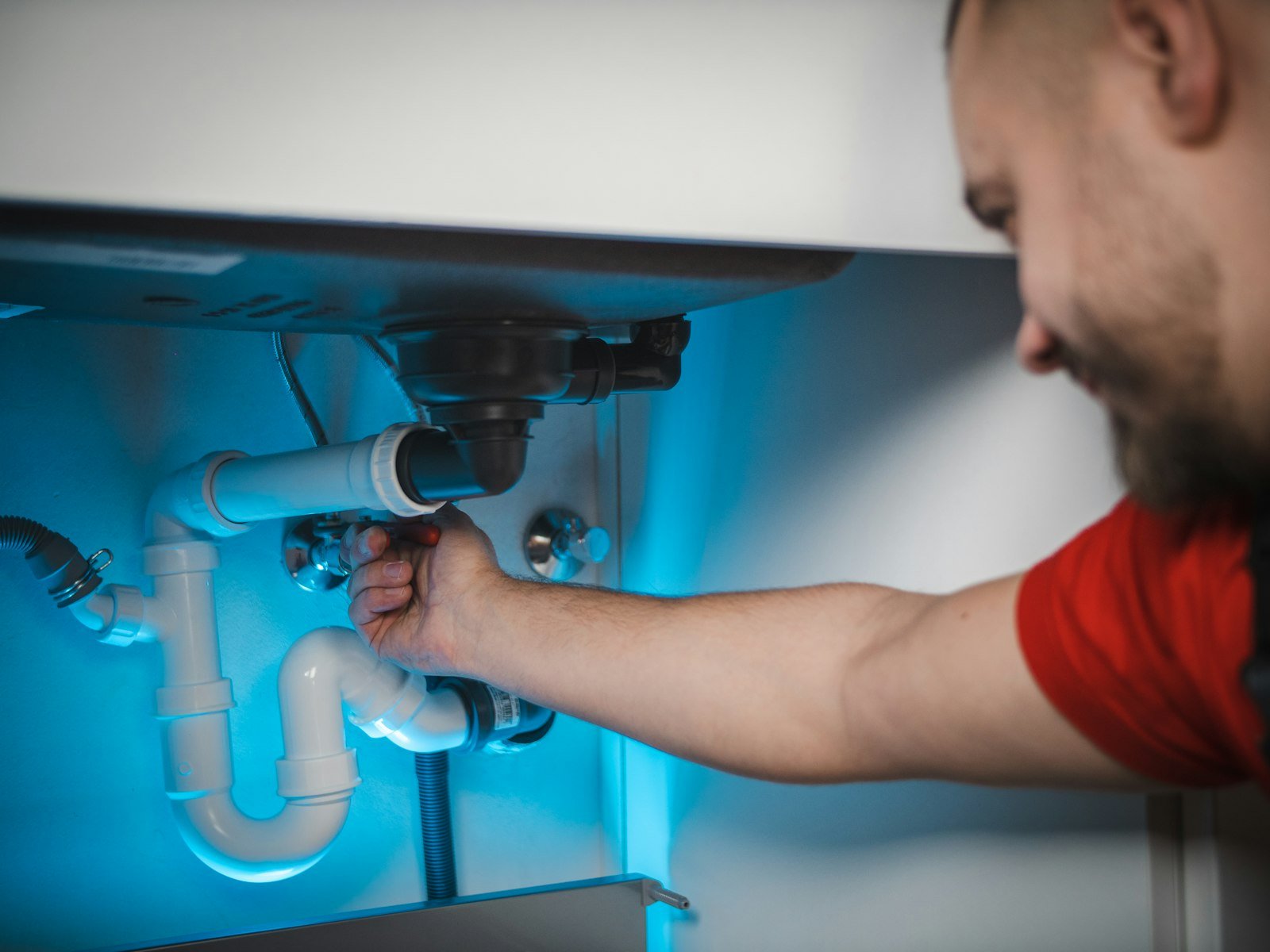 A plumber repairing pipes inside a wall cabinet